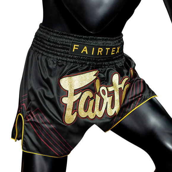 Black Fairtex Muay Thai shorts with gold and red accents on a white background