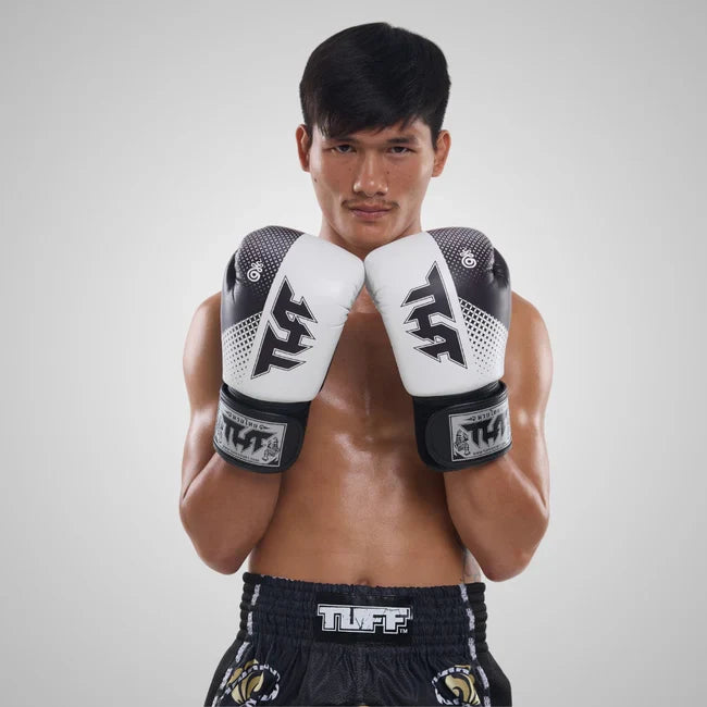 Man wearing boxing gloves and shorts with a brand logo on a plain background