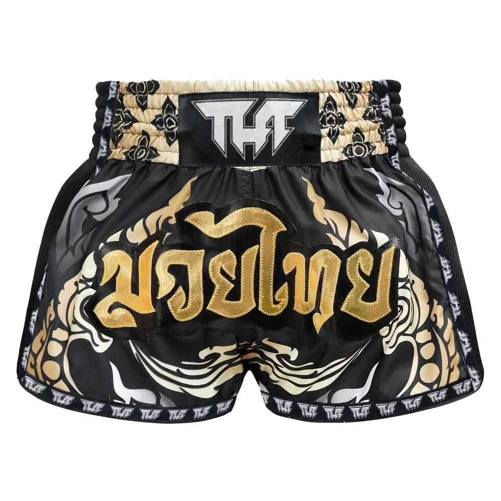 Black and gold Muay Thai shorts with decorative patterns on a white background