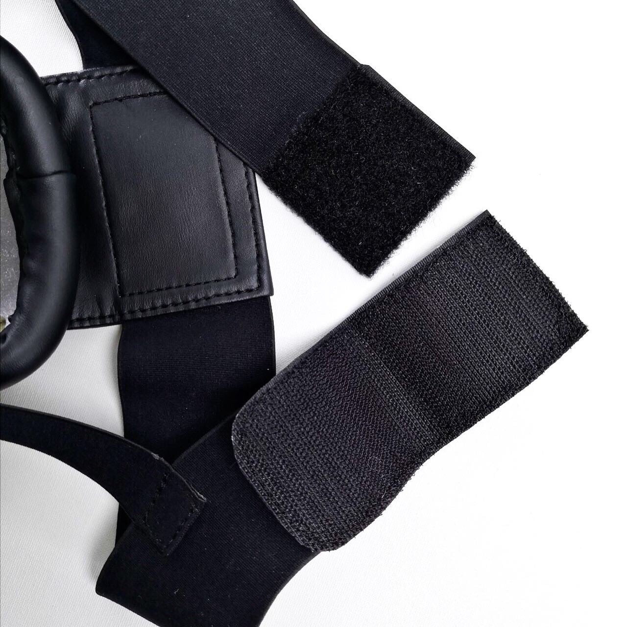 Close-up of black straps and a circular  groin guard on a white background