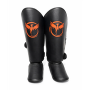 Black shin guards with orange logo on a white background
