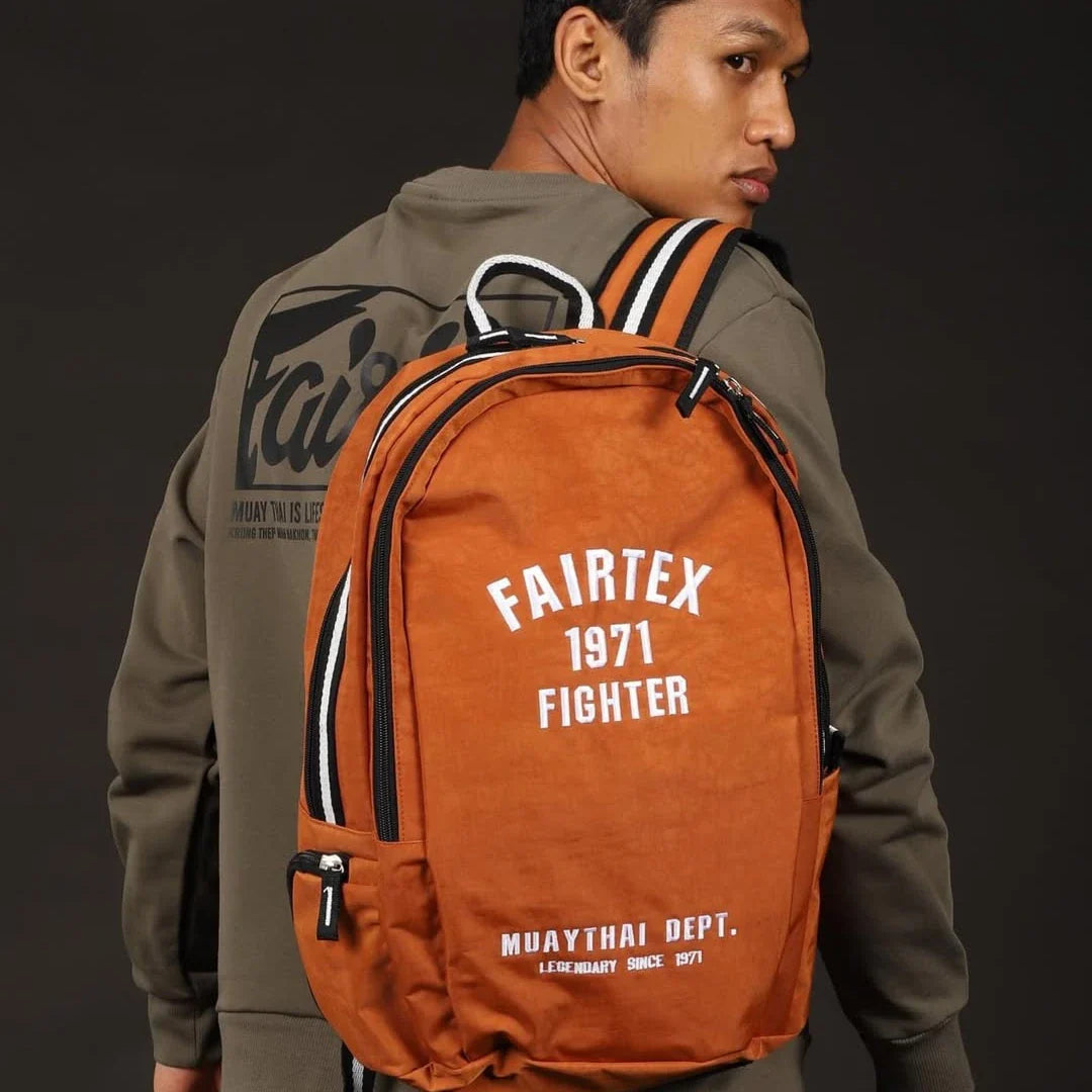 Person wearing an orange Fairtex backpack with a dark background
