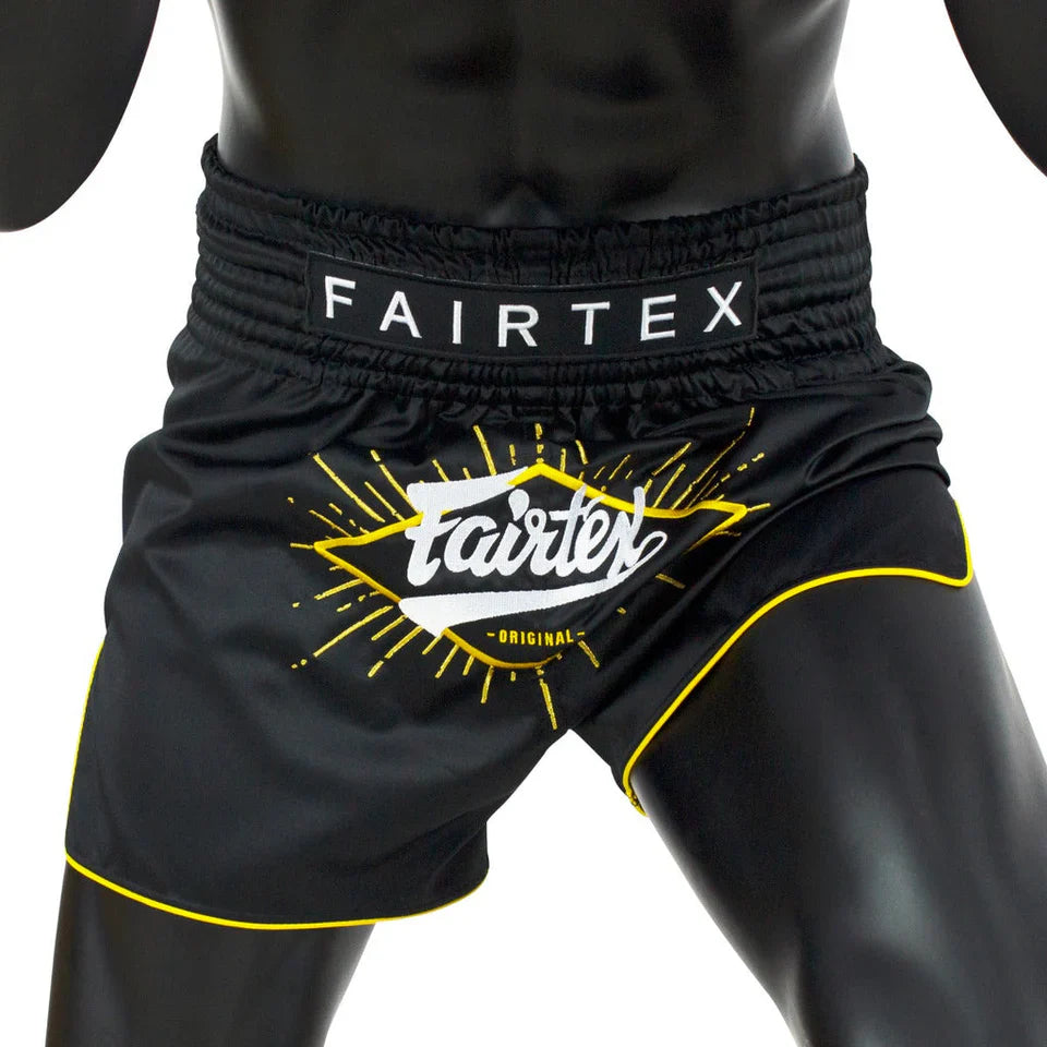 Black Fairtex Muay Thai shorts with yellow accents on a mannequin against a white background