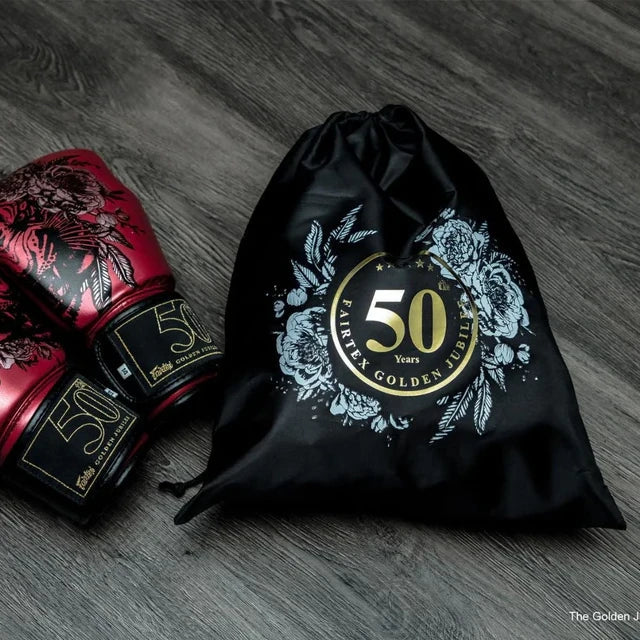 Red boxing glove with '50' logo next to a black drawstring bag with '50' logo on a wooden surface
