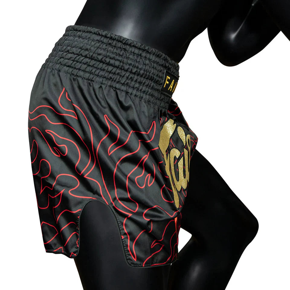 Black athletic Muay Thai shorts with red flame pattern and gold logo on a mannequin against a white background