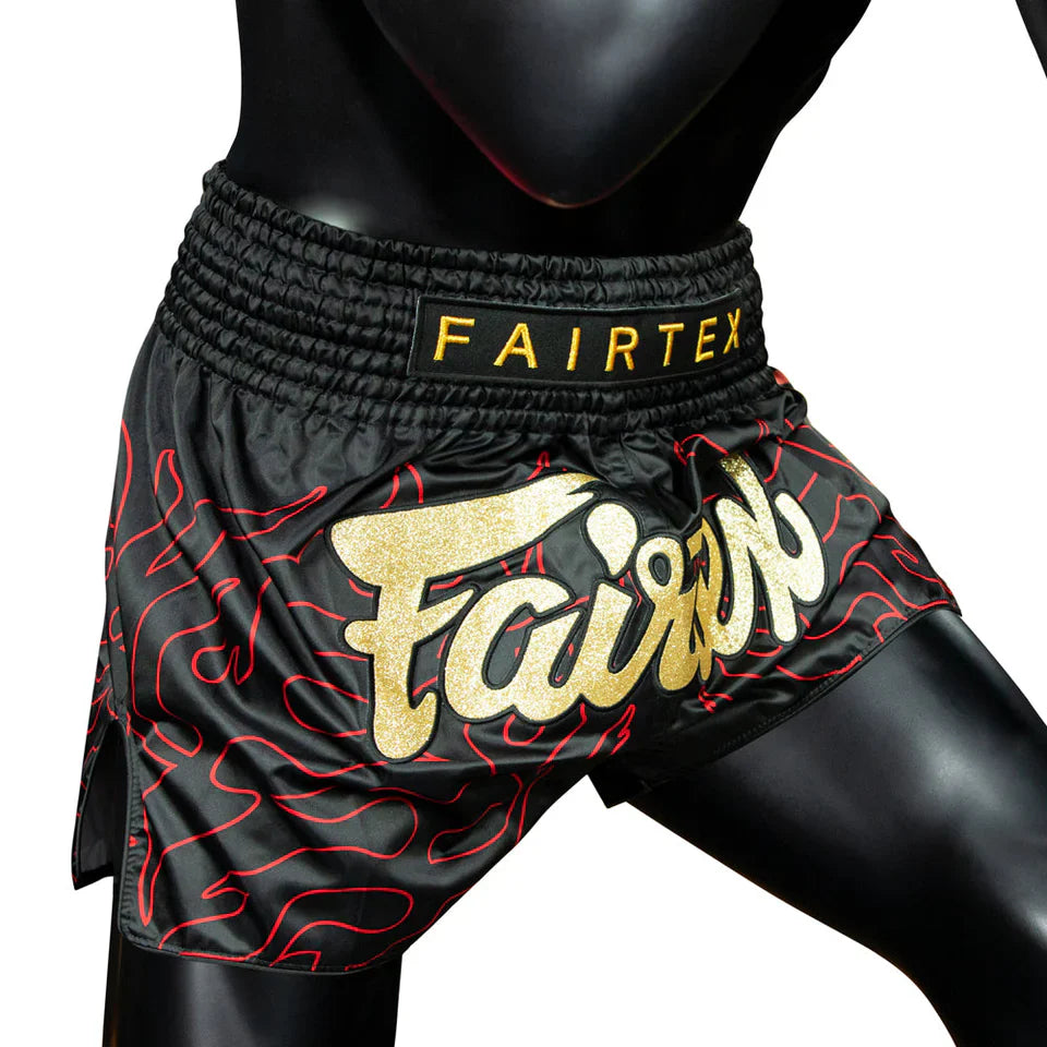 Black Muay Thai shorts with red patterns and Fairtex branding on a mannequin.