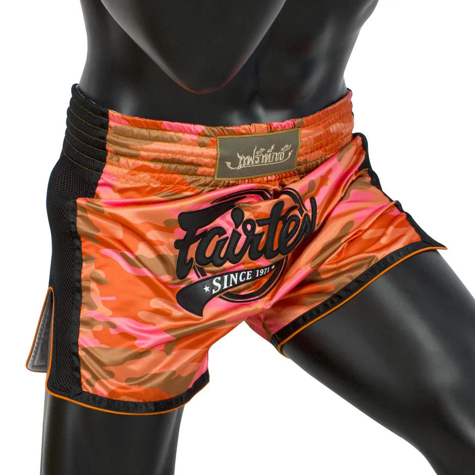 Orange and black patterned Muay Thai shorts with 'fairtex' branding on a mannequin.