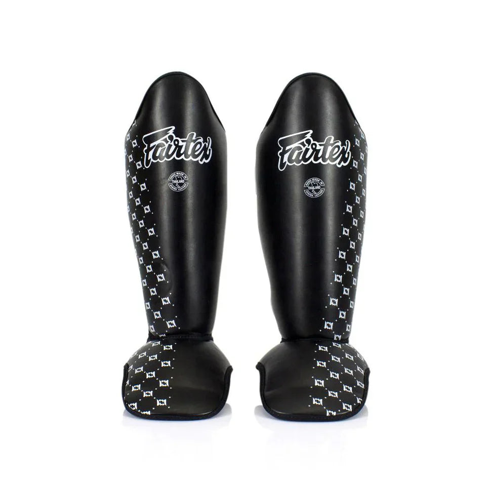 Pair of black shin guards with white patterns and 'Fairtex' branding on a white background