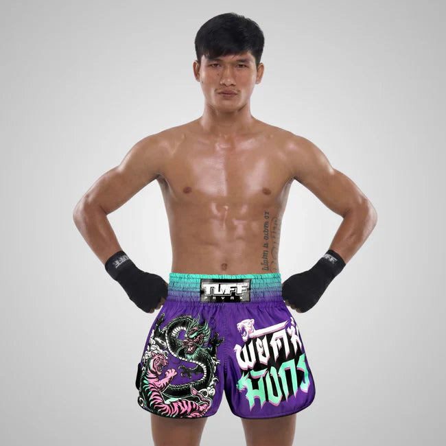 Man wearing colorful Muay Thai boxing shorts with a brand logo on a gray background